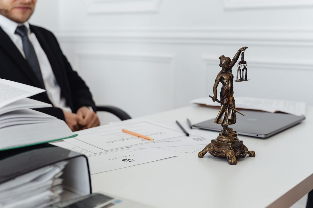 Advogado à mesa de escritório ao lado da estátua da Justiça e de documentos jurídicos