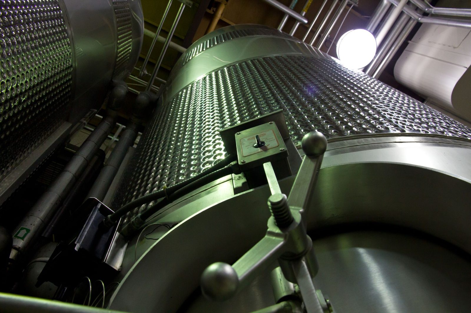 Tanques industriais de aço inox com camisas de resfriamento e tubulações em galpão, sem pessoas, evocando o ambiente industrial pesado e frio do trabalho na agroindústria de carnes