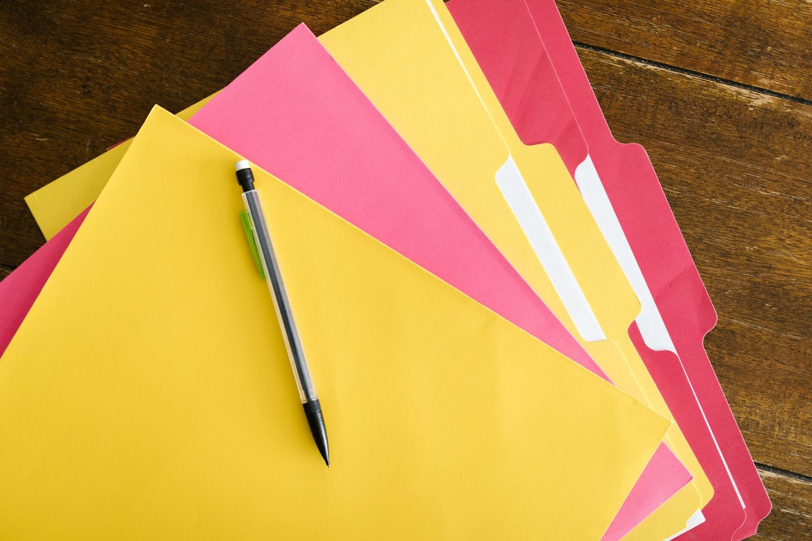 Pastas de documentos coloridas e caneta, remetendo a contratos de prestacao de servicos