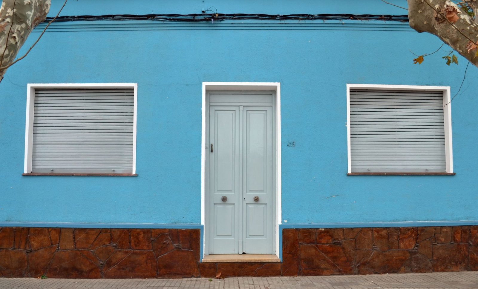 Fachada de uma casa simples de rua, com porta fechada e janelas, sem pessoas, representando o domicílio onde a visita do Cadastro Único é exigida