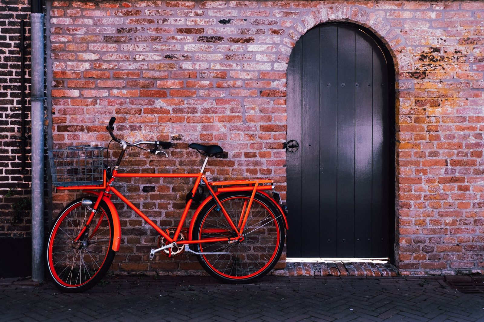 Bicicleta de carga com cesto, estacionada encostada em muro de tijolos, sem pessoas, instrumento de trabalho do entregador de aplicativo