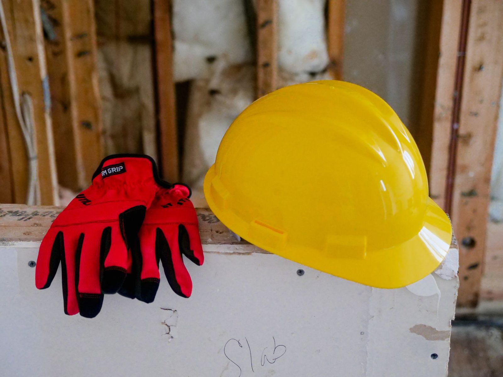 Capacete de segurança amarelo e par de luvas de proteção apoiados sobre superfície de obra, sem pessoas, equipamentos de proteção individual do ambiente de trabalho