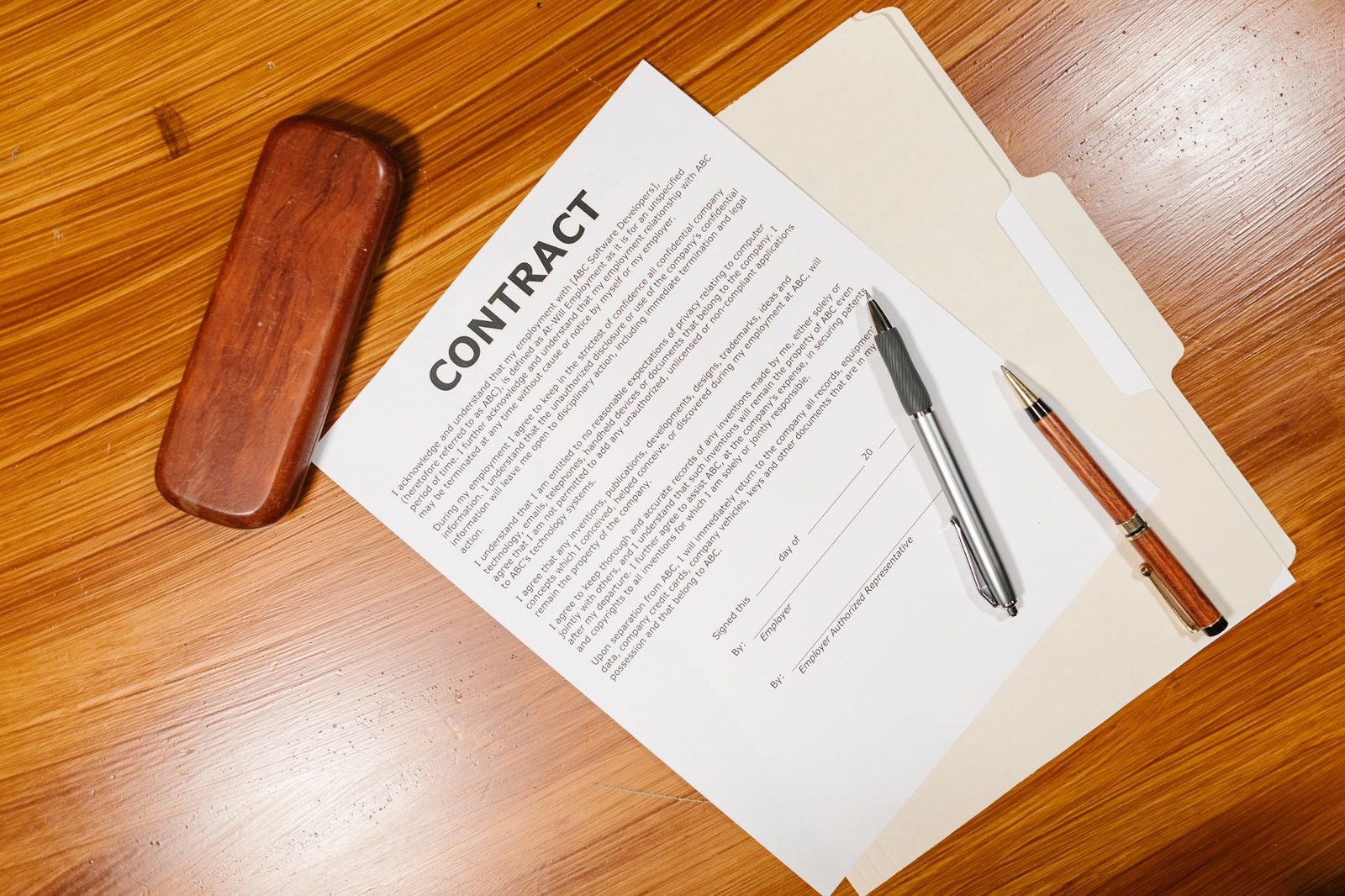 Documento de contrato de trabalho ao lado de canetas e uma pasta de arquivo sobre mesa de madeira, sem pessoas, representando a petição e os documentos do processo
