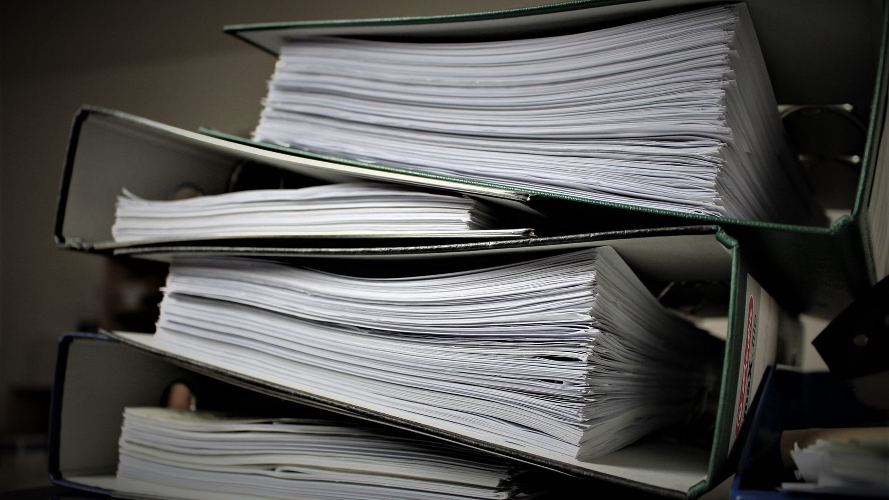 Pilha de pastas de arquivo lotadas de documentos, empilhadas sobre uma mesa, sem pessoas.