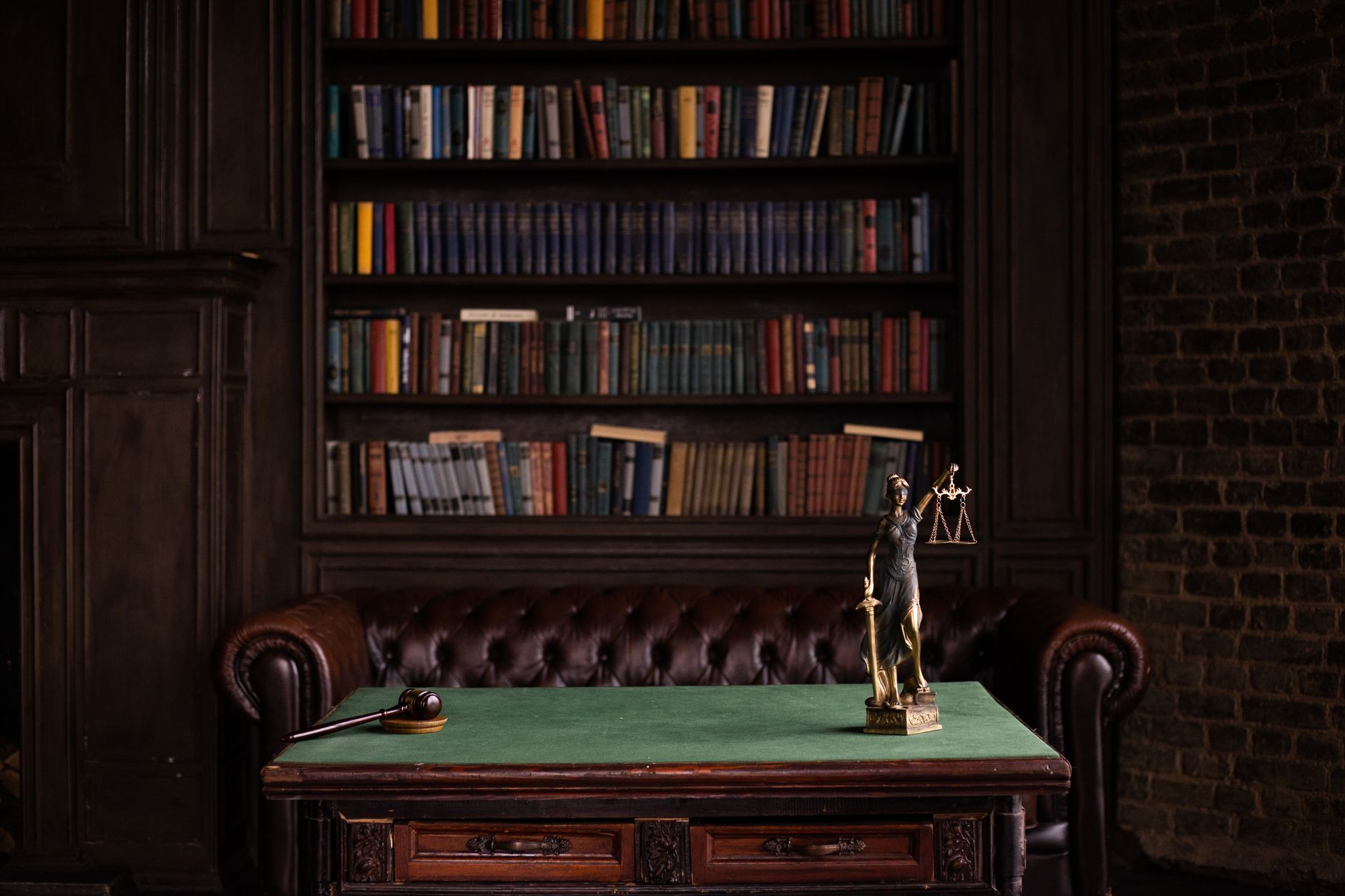 Estante de livros jurídicos e estatueta da Justiça sobre a mesa, foto sóbria, sem pessoas.