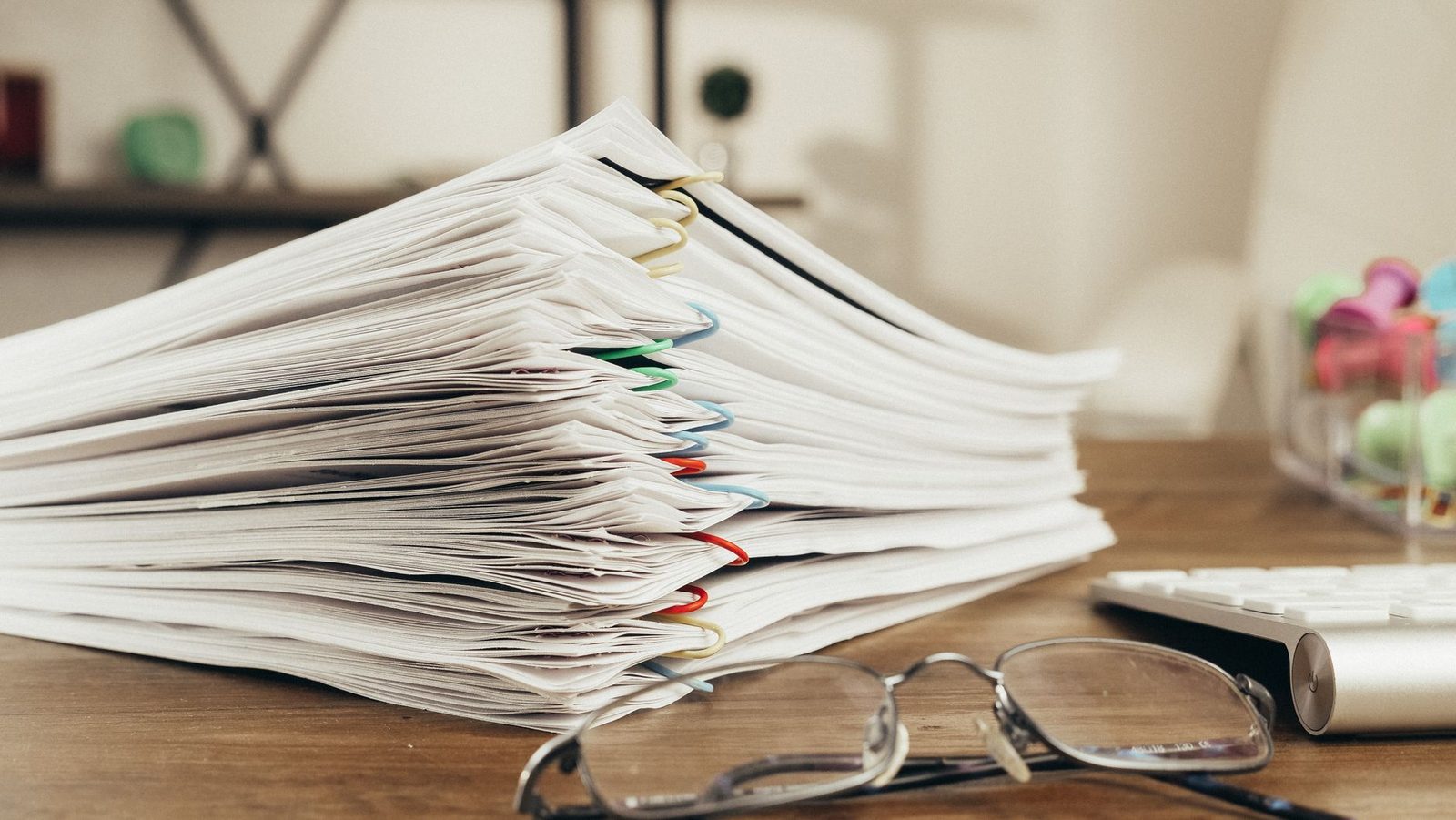 Pilha de documentos e óculos sobre a mesa, remetendo à análise de benefícios do INSS