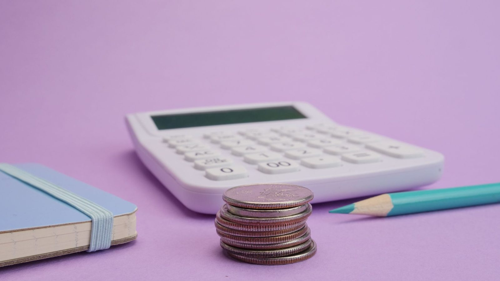 Calculadora, moedas empilhadas e caderno para cálculo de valores